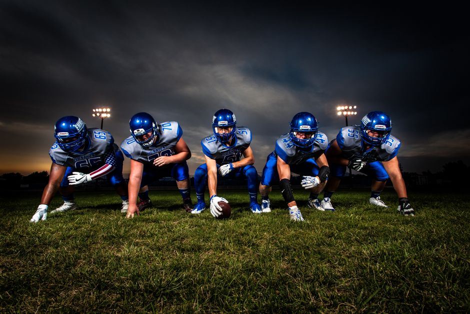 A cohesive football team lines up on the field under stadium lights, prepared for the game ahead.